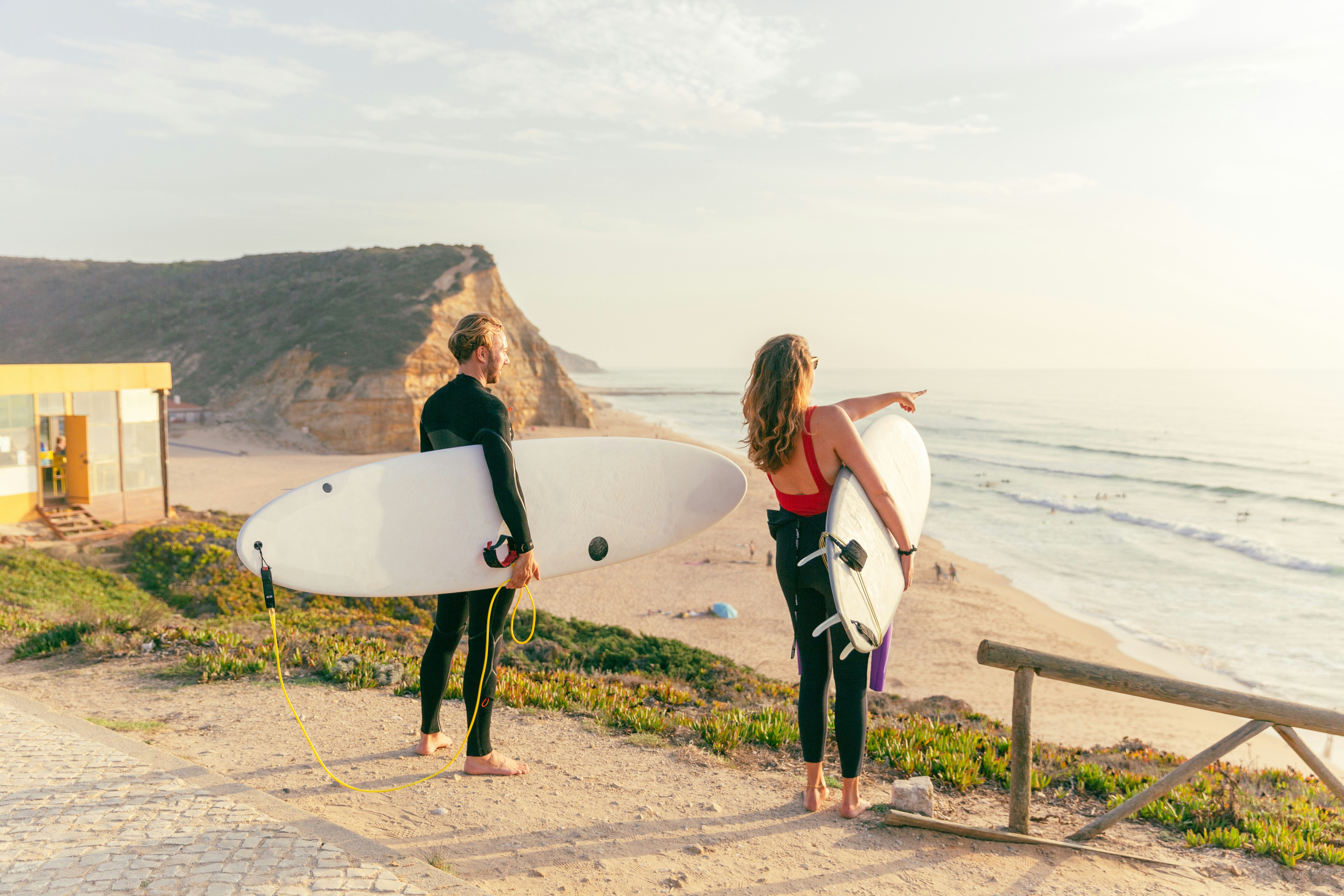 Two surfers looking at the ocean from a cliff at sunset