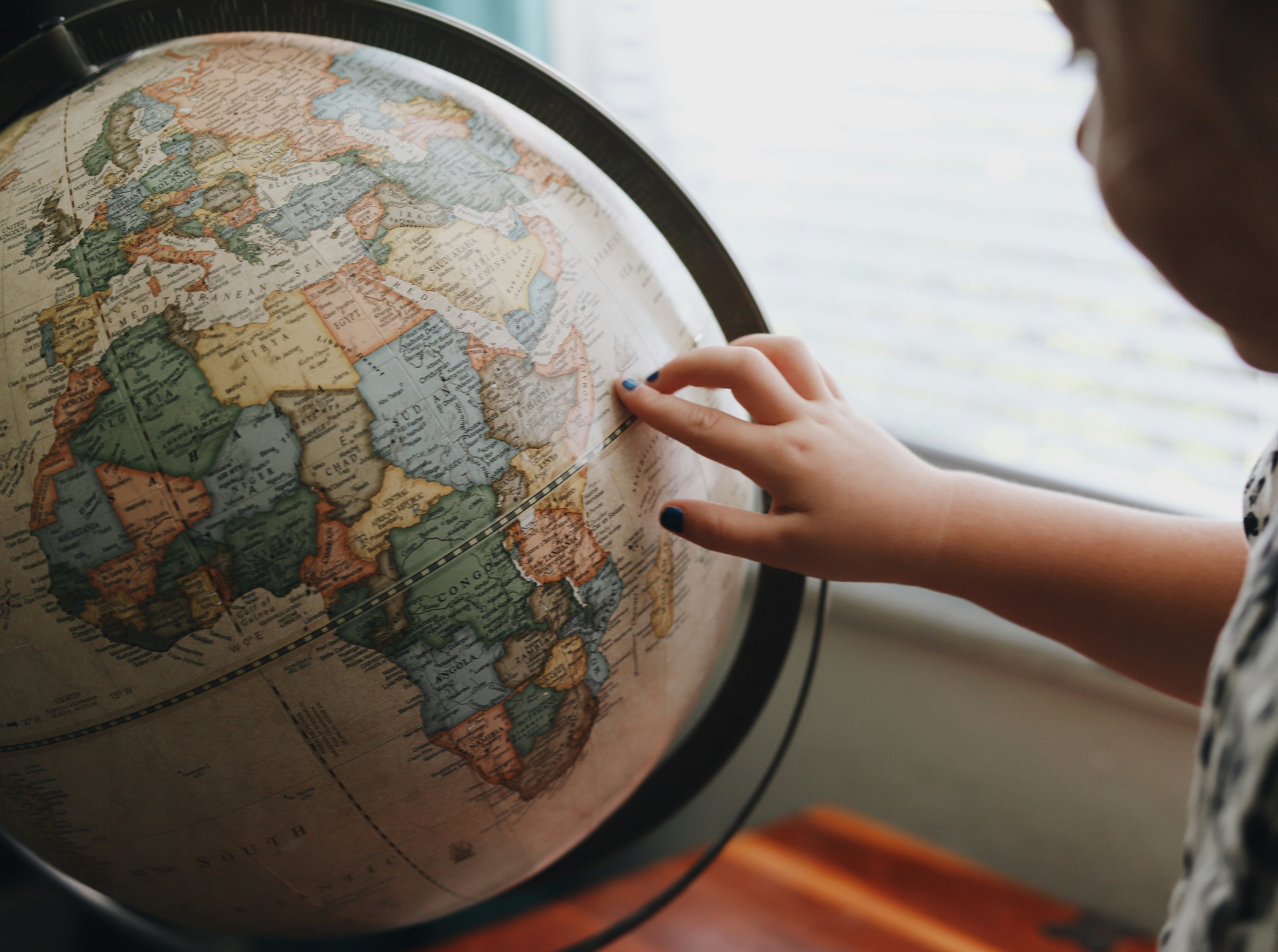 A finger traces a path across Europe and the Mediterranean on a vintage globe