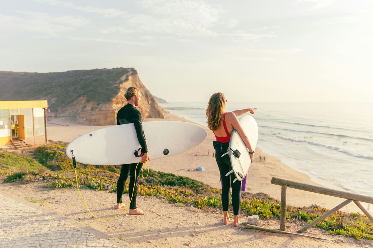 Two surfers looking at the ocean from a cliff at sunset